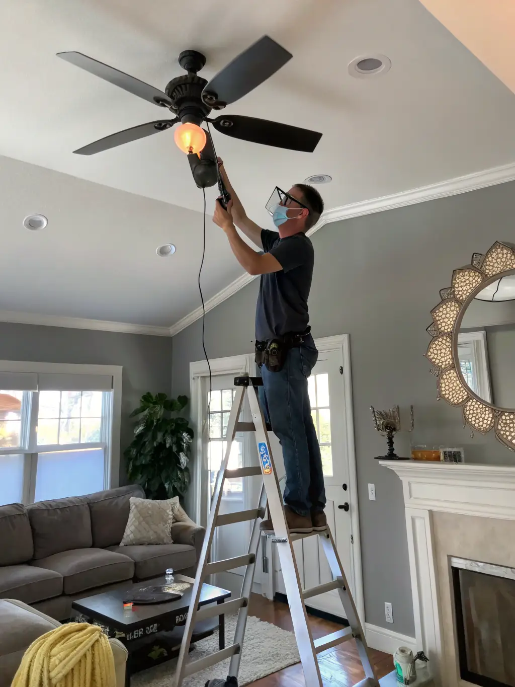 An electrician is replacing an old, outdated ceiling fan with a new, energy-efficient model in a customer's home, improving energy savings.