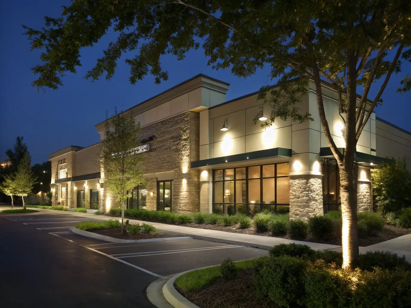 A wide shot of a commercial building's exterior, showcasing newly installed landscape lighting that enhances security and aesthetic appeal.